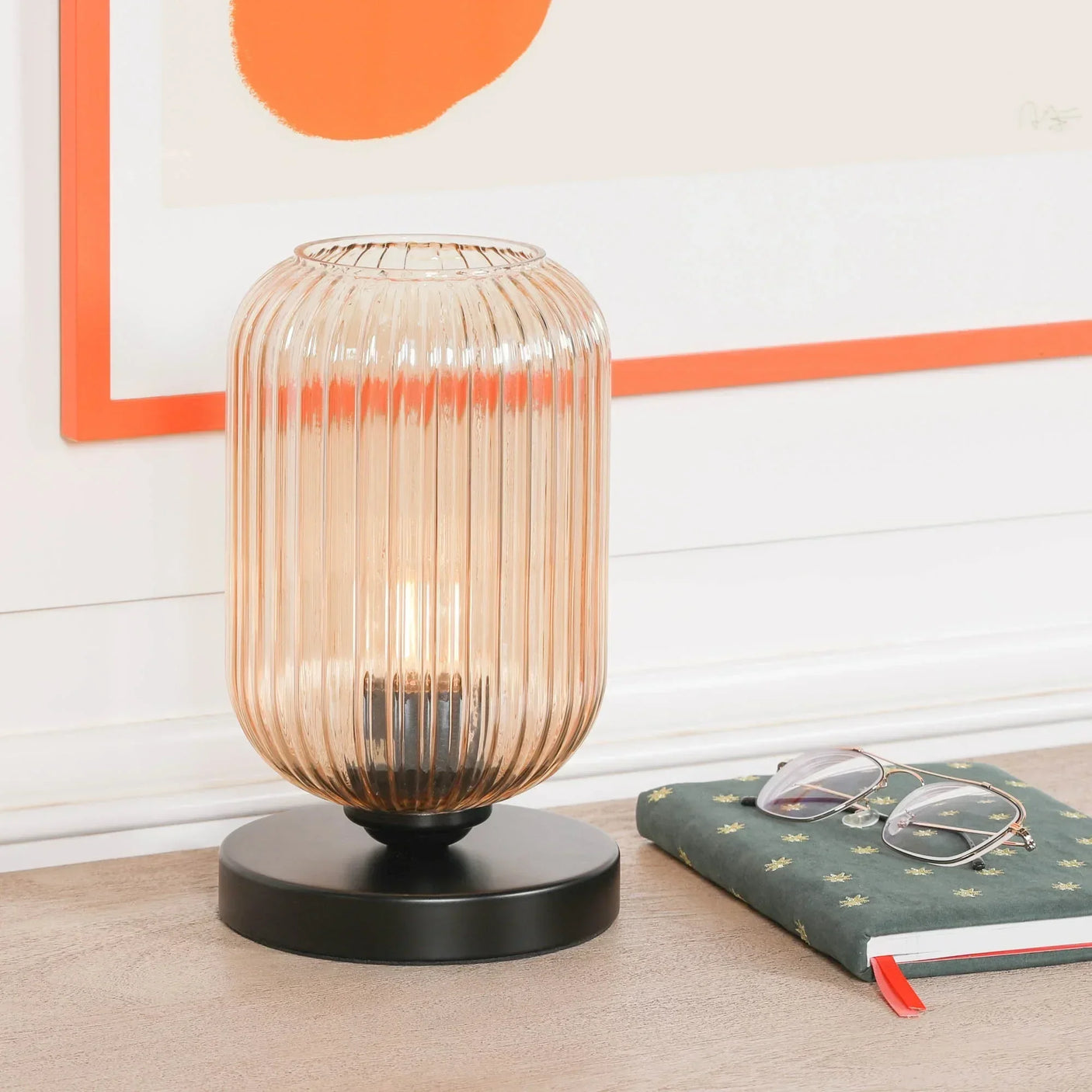 Ribbed glass table lamp with black base on wooden surface beside notebook and glasses