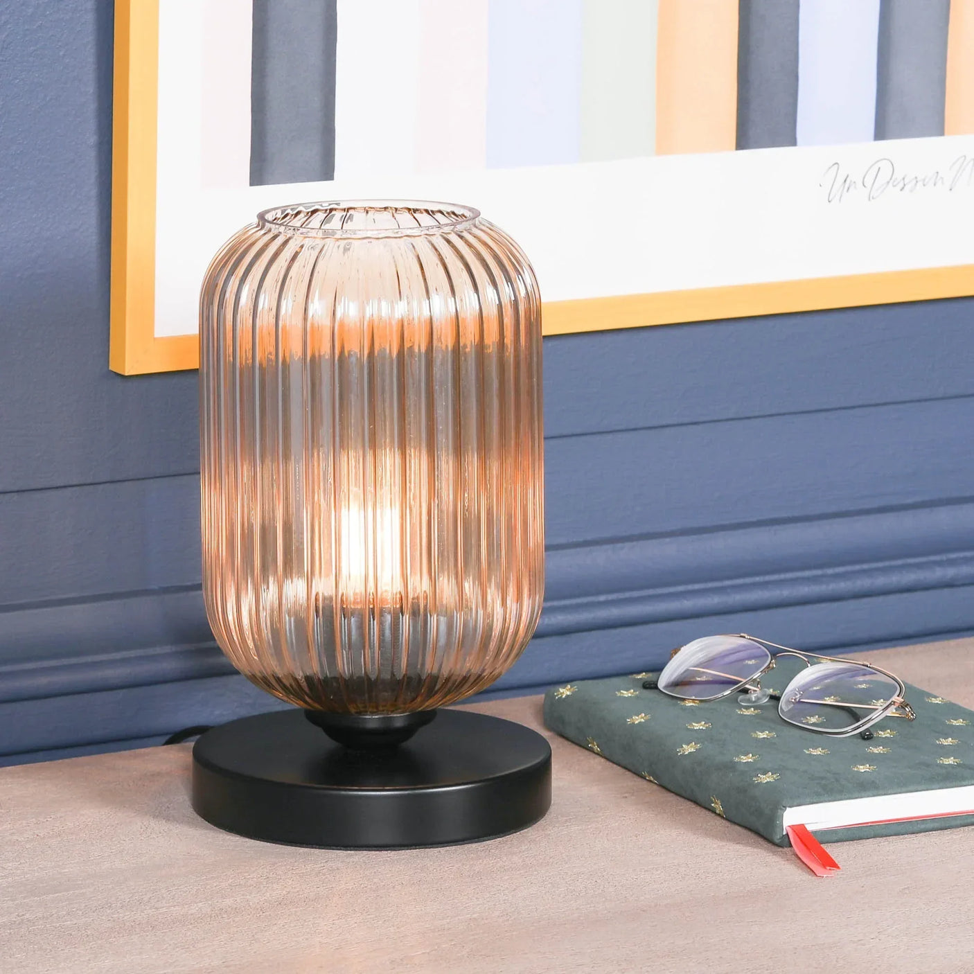 Amber glass table lamp with ribbed shade and black base on wooden surface