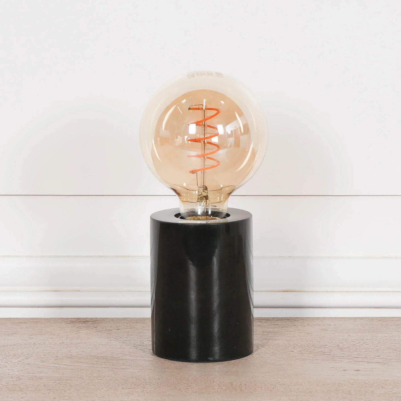 table lamp with round amber bulb and black cylindrical base on wooden surface