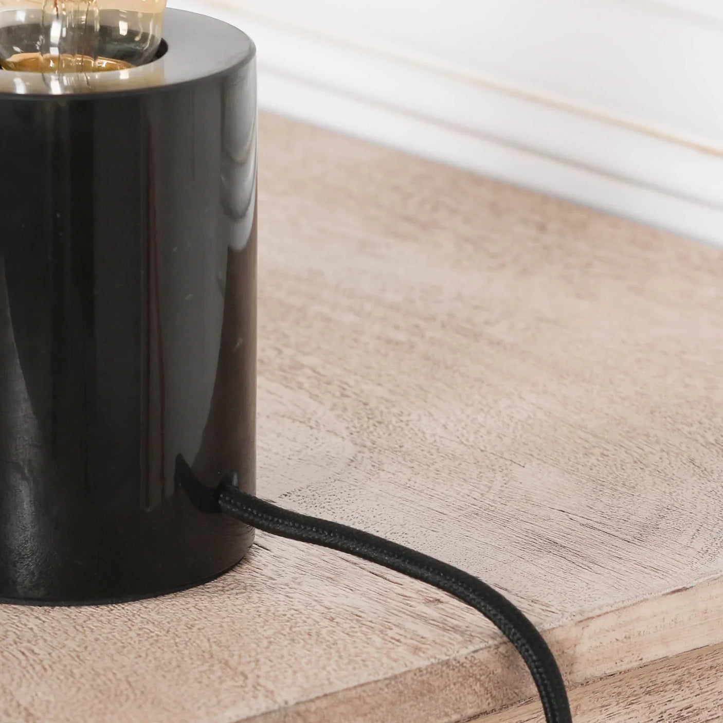 Black cylindrical table lamp base with cord on light wood surface