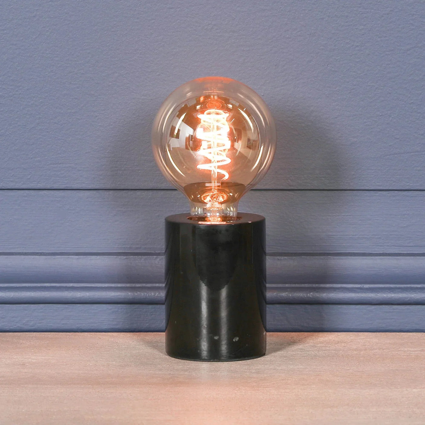 Modern table lamp with exposed filament bulb and black marble base against blue wall