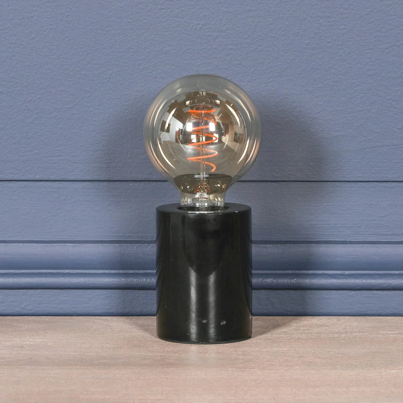 Modern table lamp with round clear bulb and black cylindrical base on wooden surface