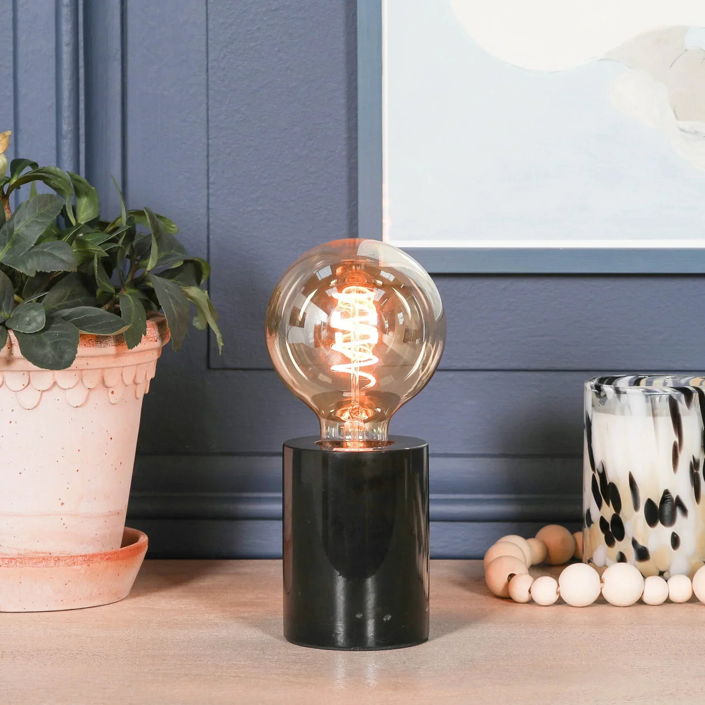 Modern table lamp with exposed filament bulb on black marble base, styled on a wooden surface