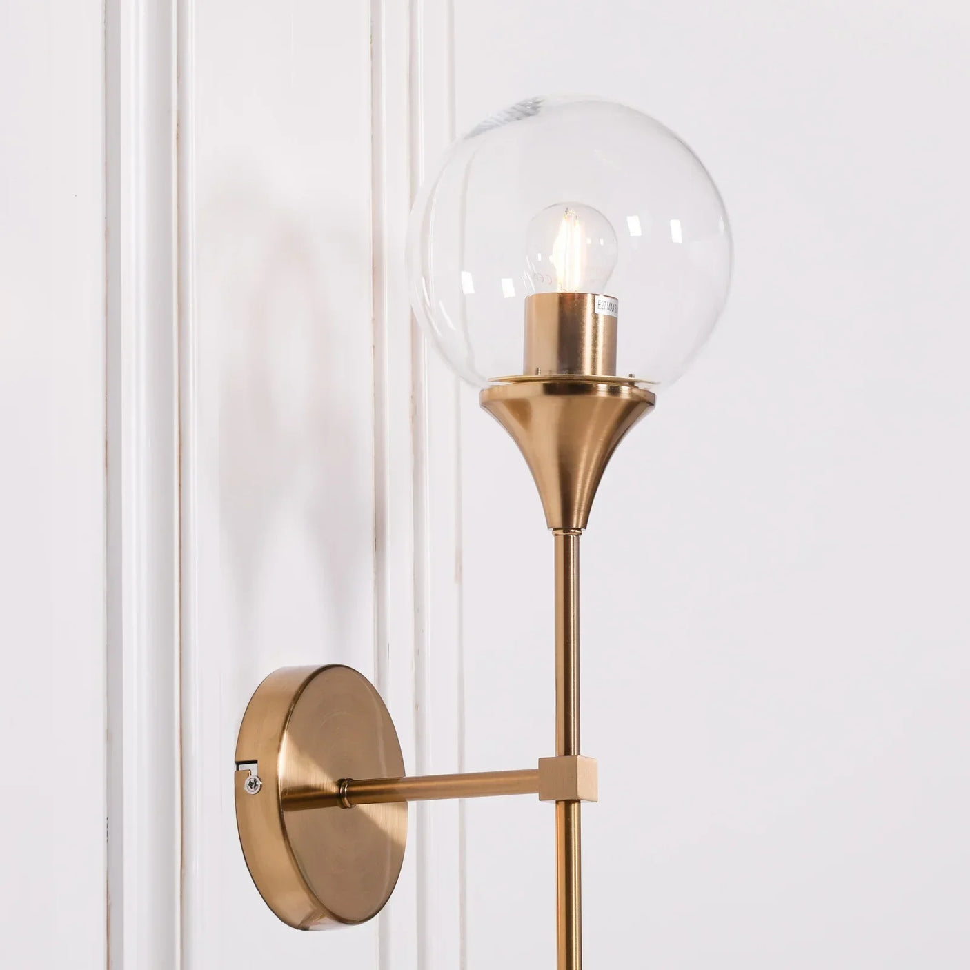 Modern wall sconce with gold metal frame and clear glass globe shade on white wall