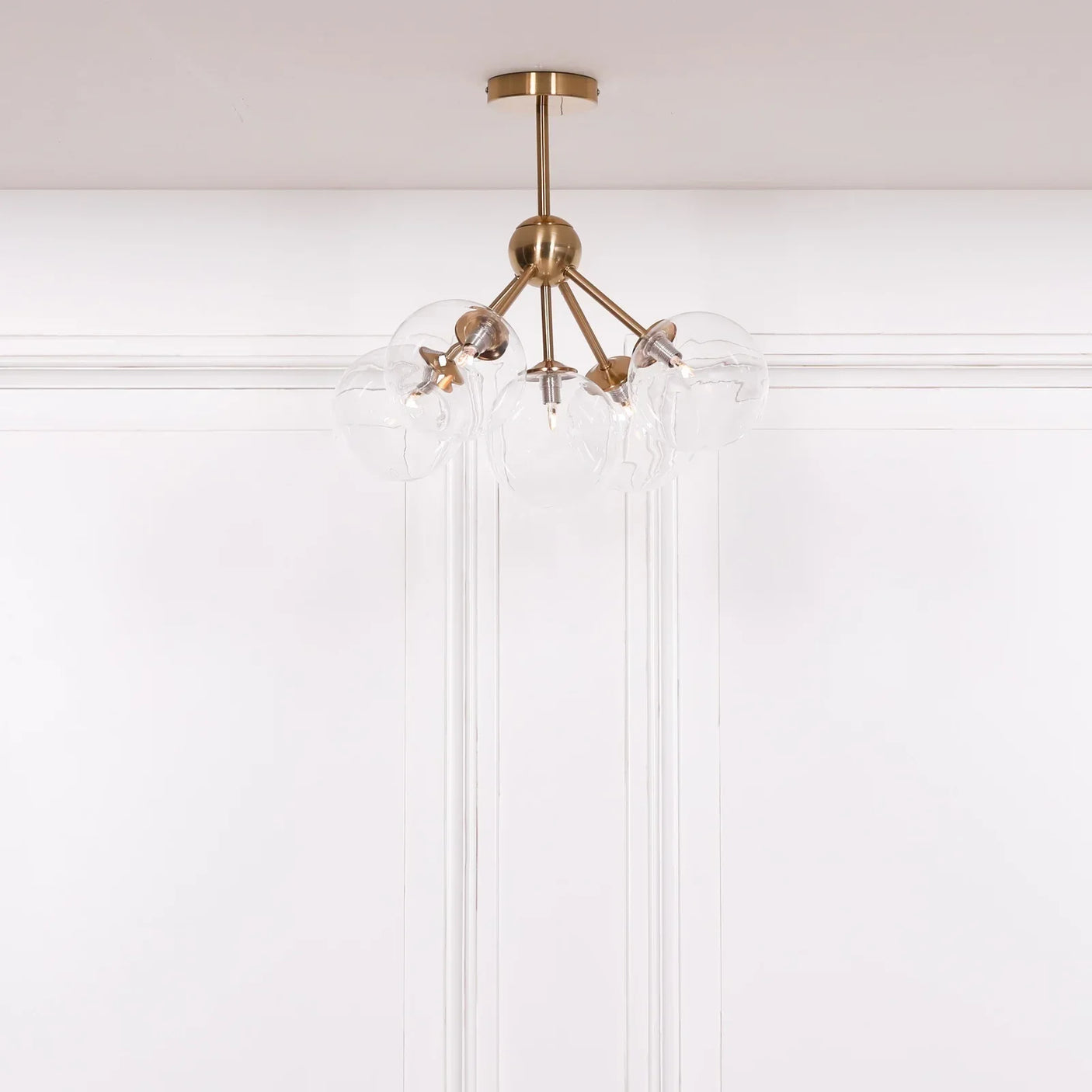 Brass ceiling light fixture with six clear glass globe shades against white panelled wall