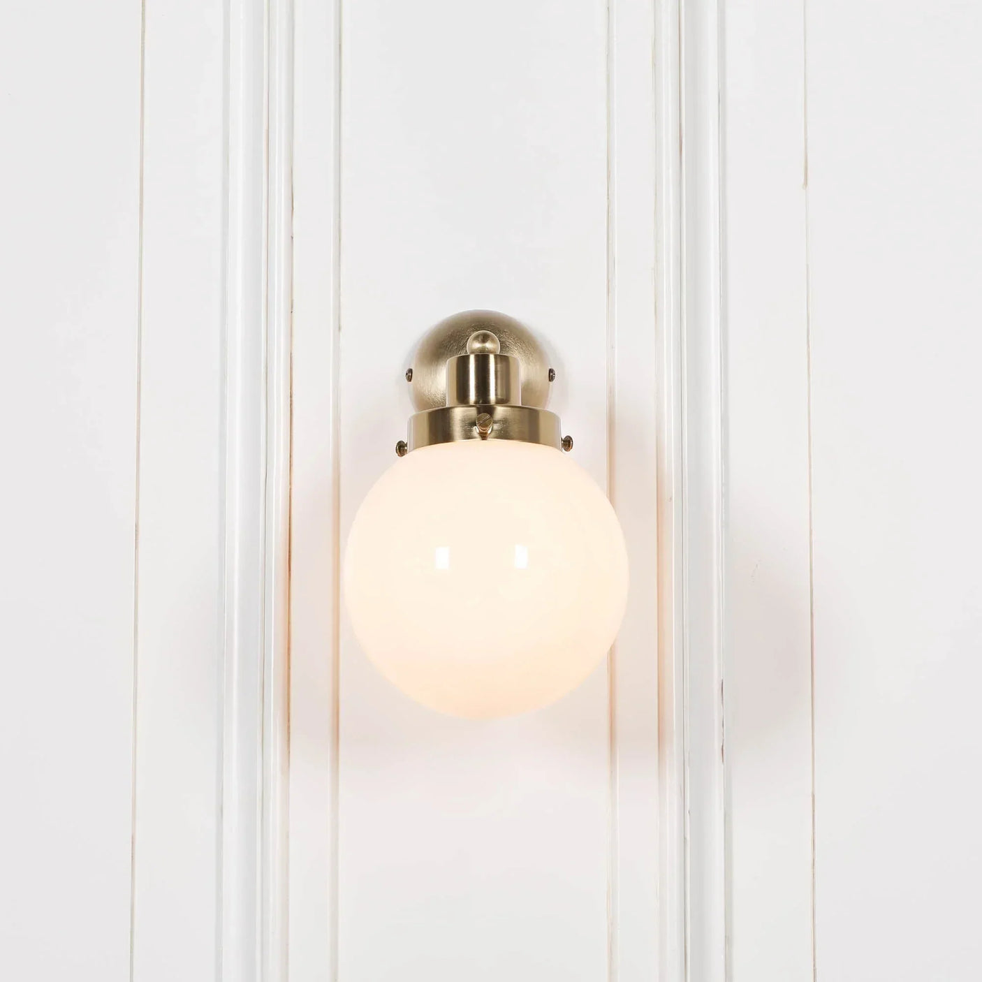 Brass wall light with frosted glass globe shade mounted on white panelled wall