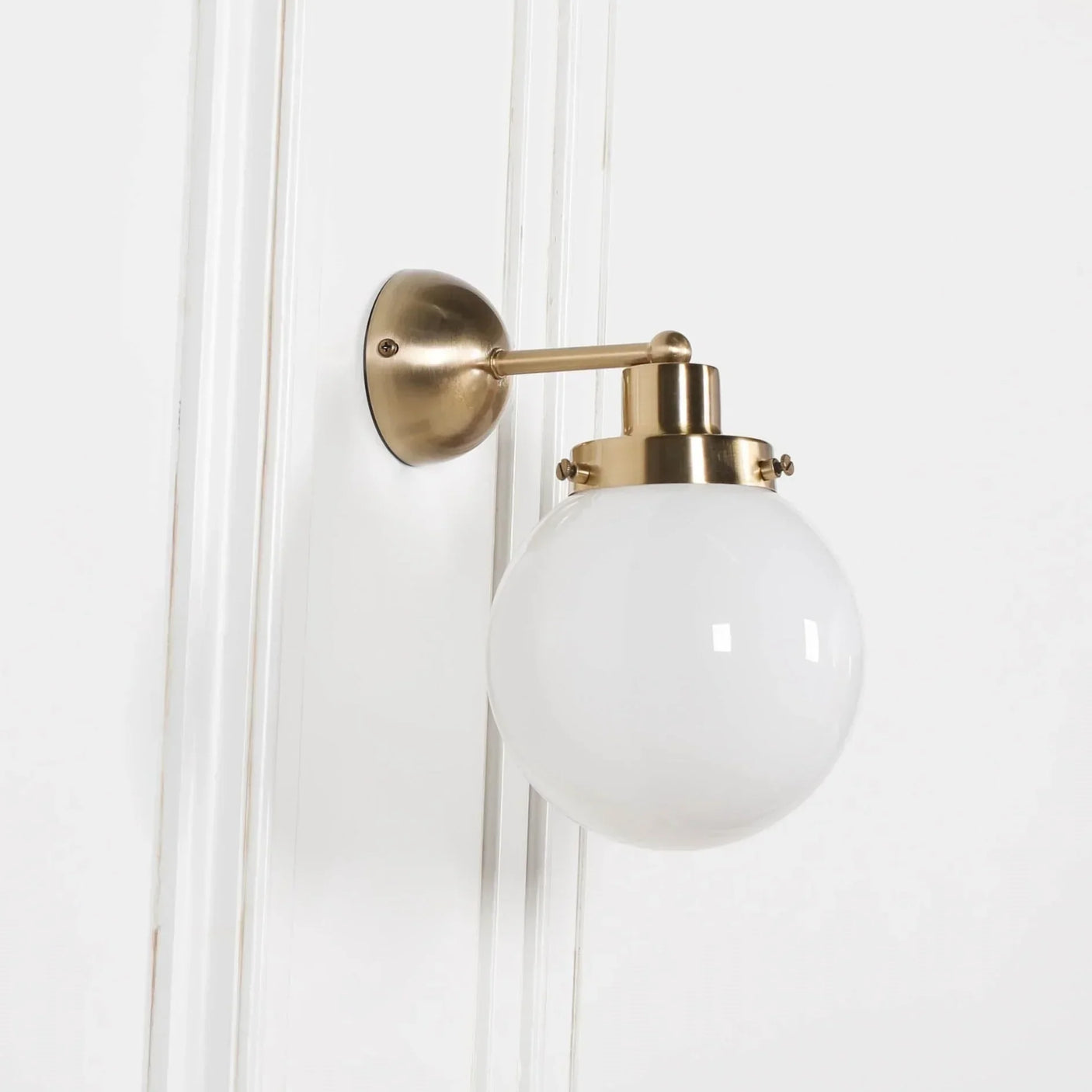Brass wall light with round white glass shade mounted on white wall panel