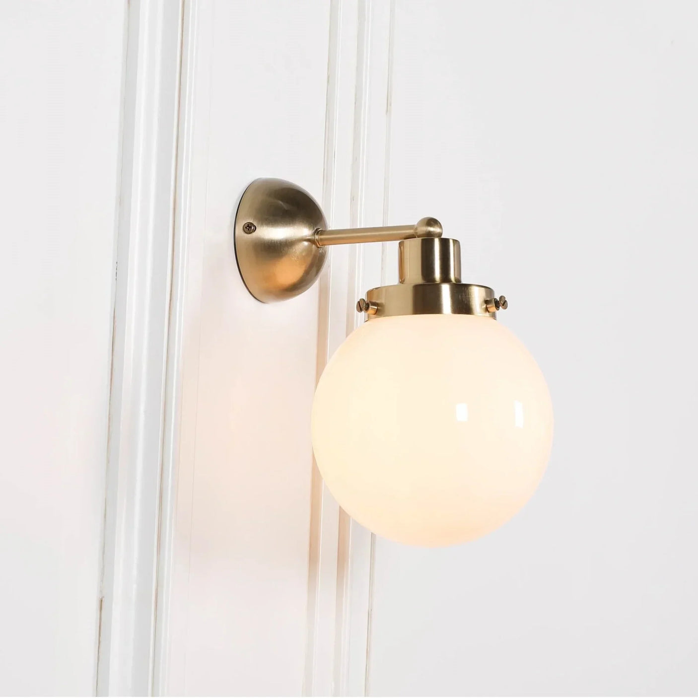 Brass wall light with round frosted glass shade mounted on white panelled wall
