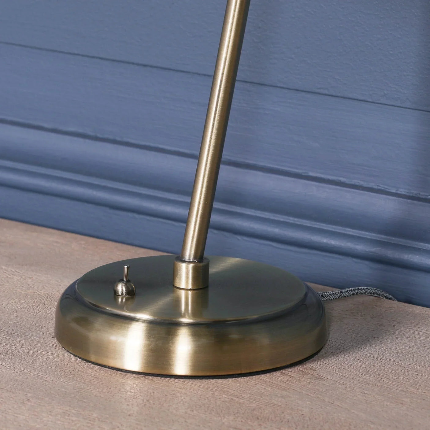 Brass table lamp base with toggle switch on wooden surface against blue wall