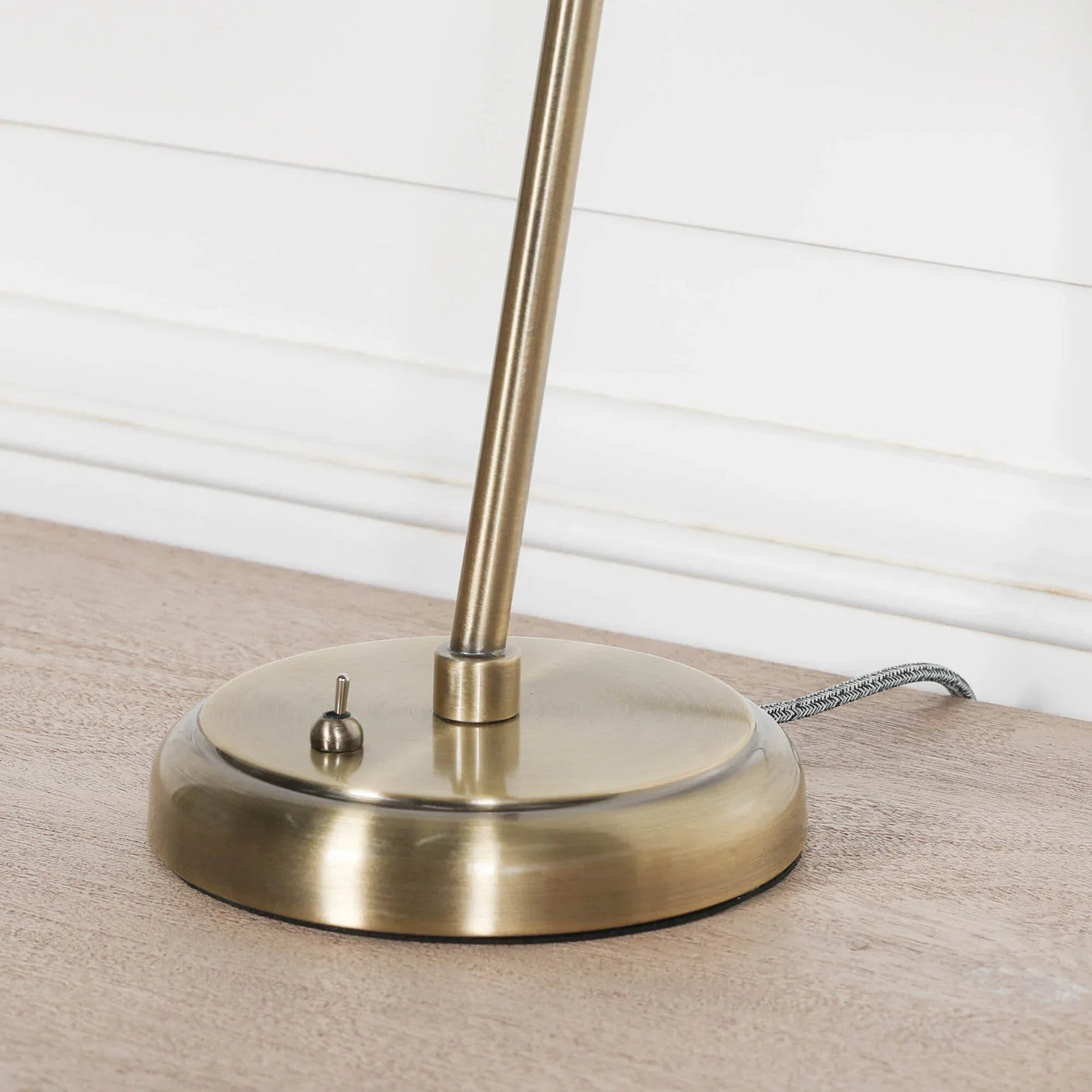 Brushed brass table lamp base with toggle switch on wooden surface