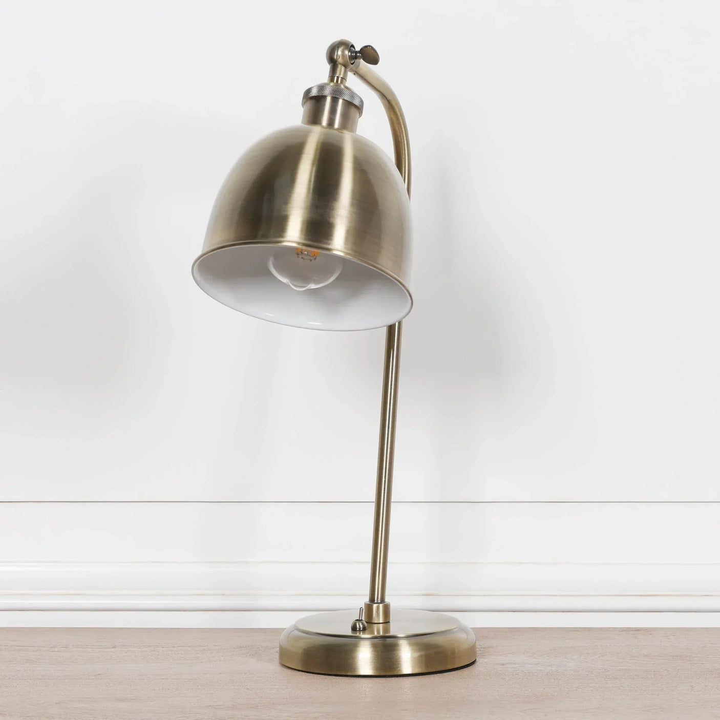 Brushed brass table lamp with dome shade on wooden surface against white wall