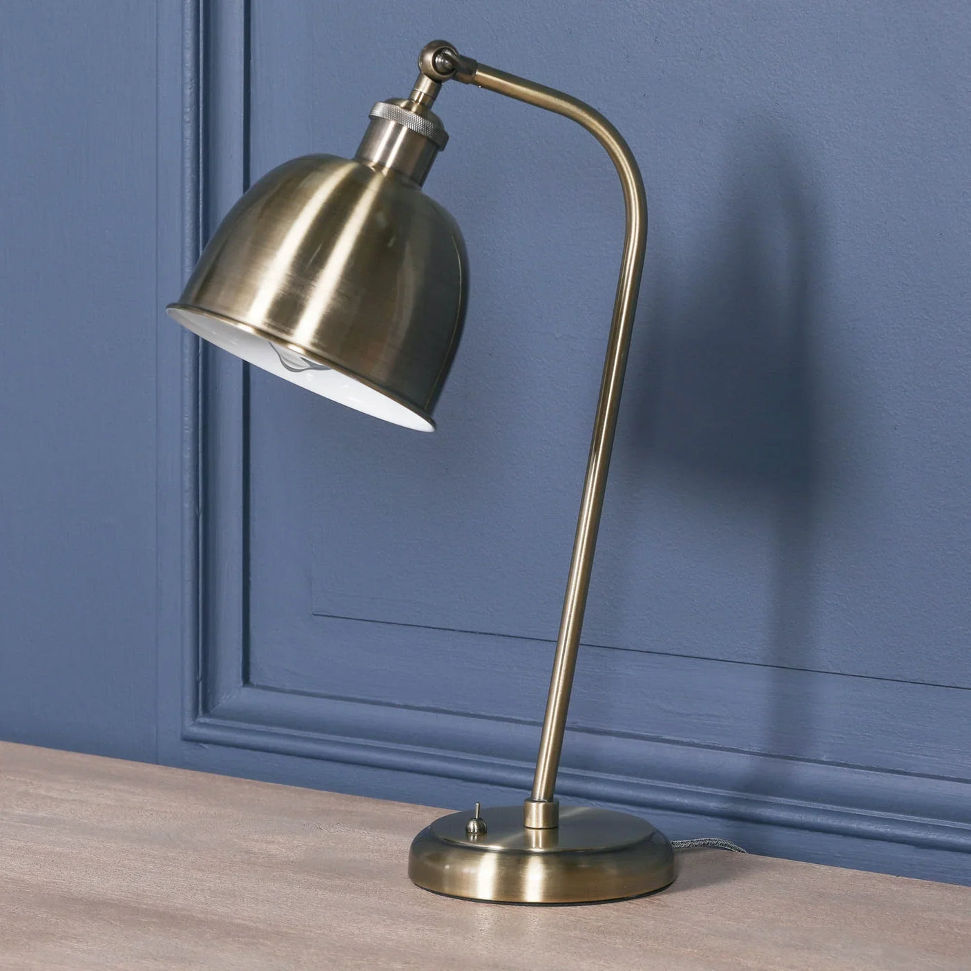 Brass desk lamp with adjustable dome shade on a wooden table against blue wall