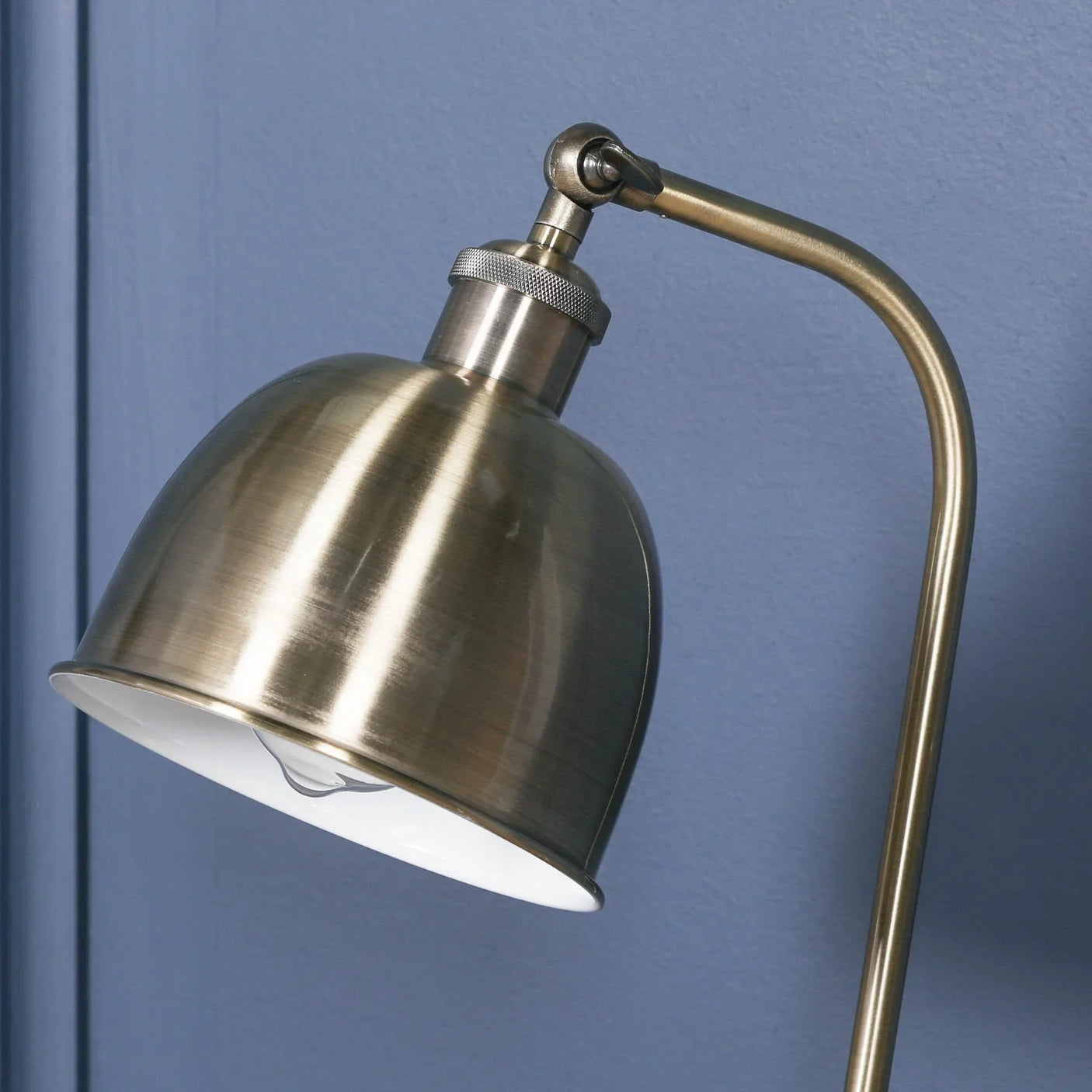 Brushed brass desk lamp with dome shade against blue wall