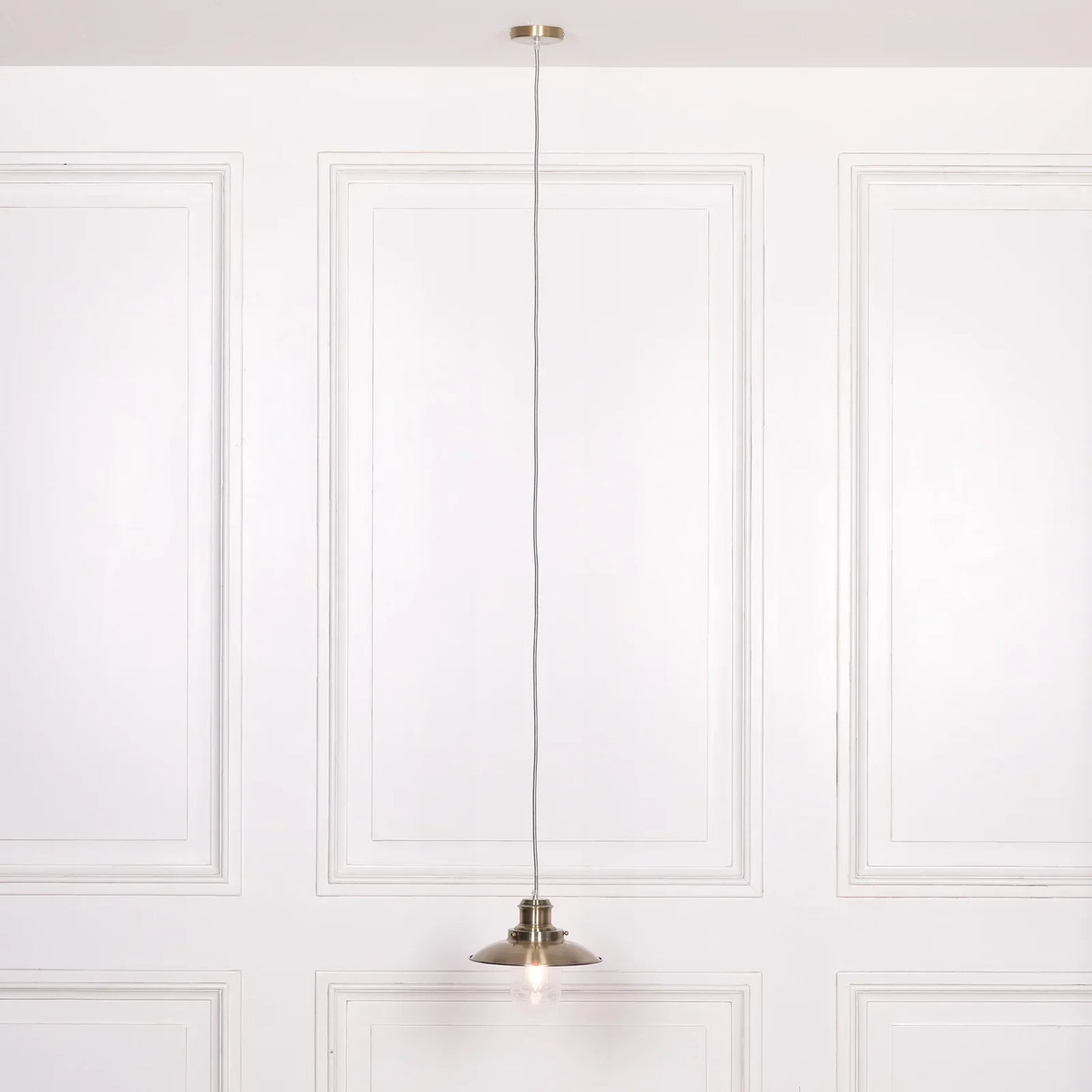Brushed metal pendant ceiling light with exposed bulb against white paneled wall