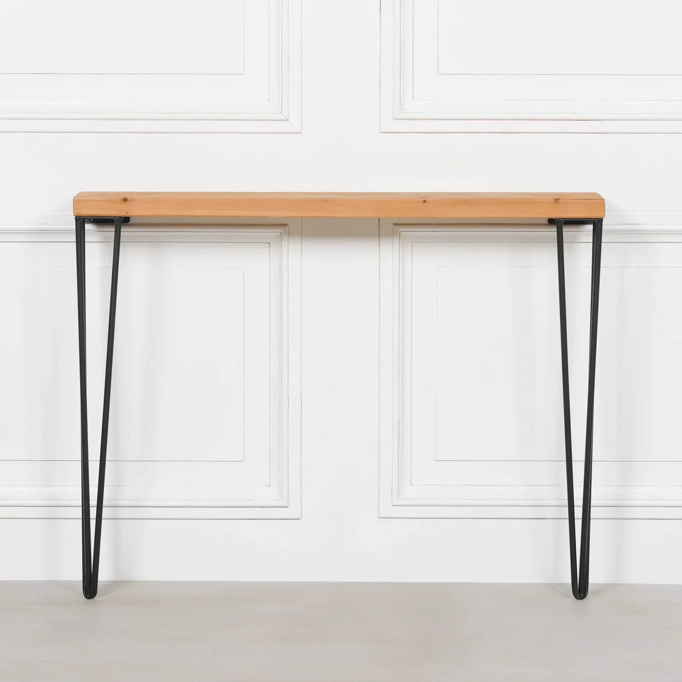 Slim console table with natural wood top and black metal hairpin legs against white wall