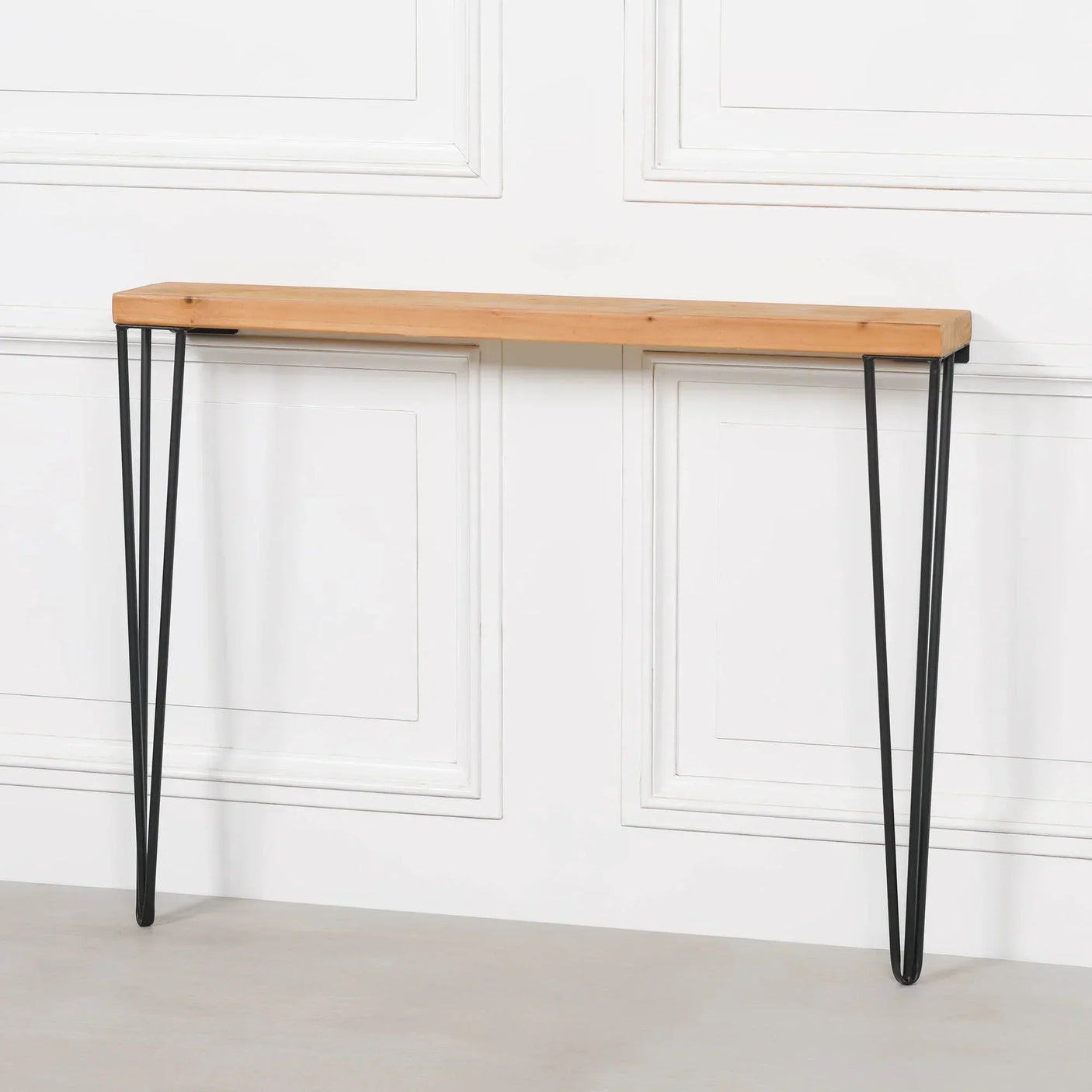 Wood console table with black metal hairpin legs against white panelled wall
