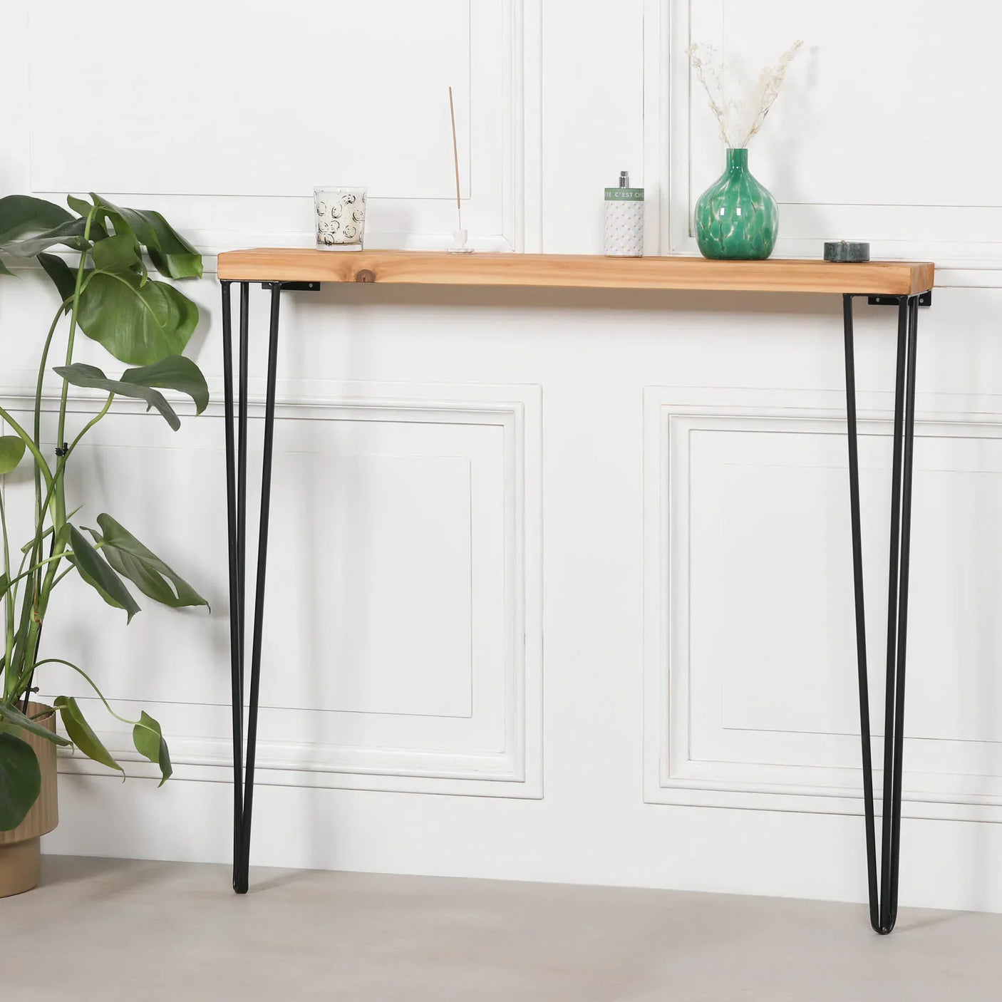 Wood console table with black metal hairpin legs against white wall, decorated with vase and plant