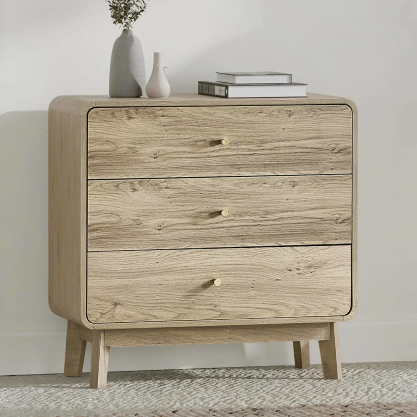 Light oak chest of drawers with three drawers, brass knobs, and decorative vases on top