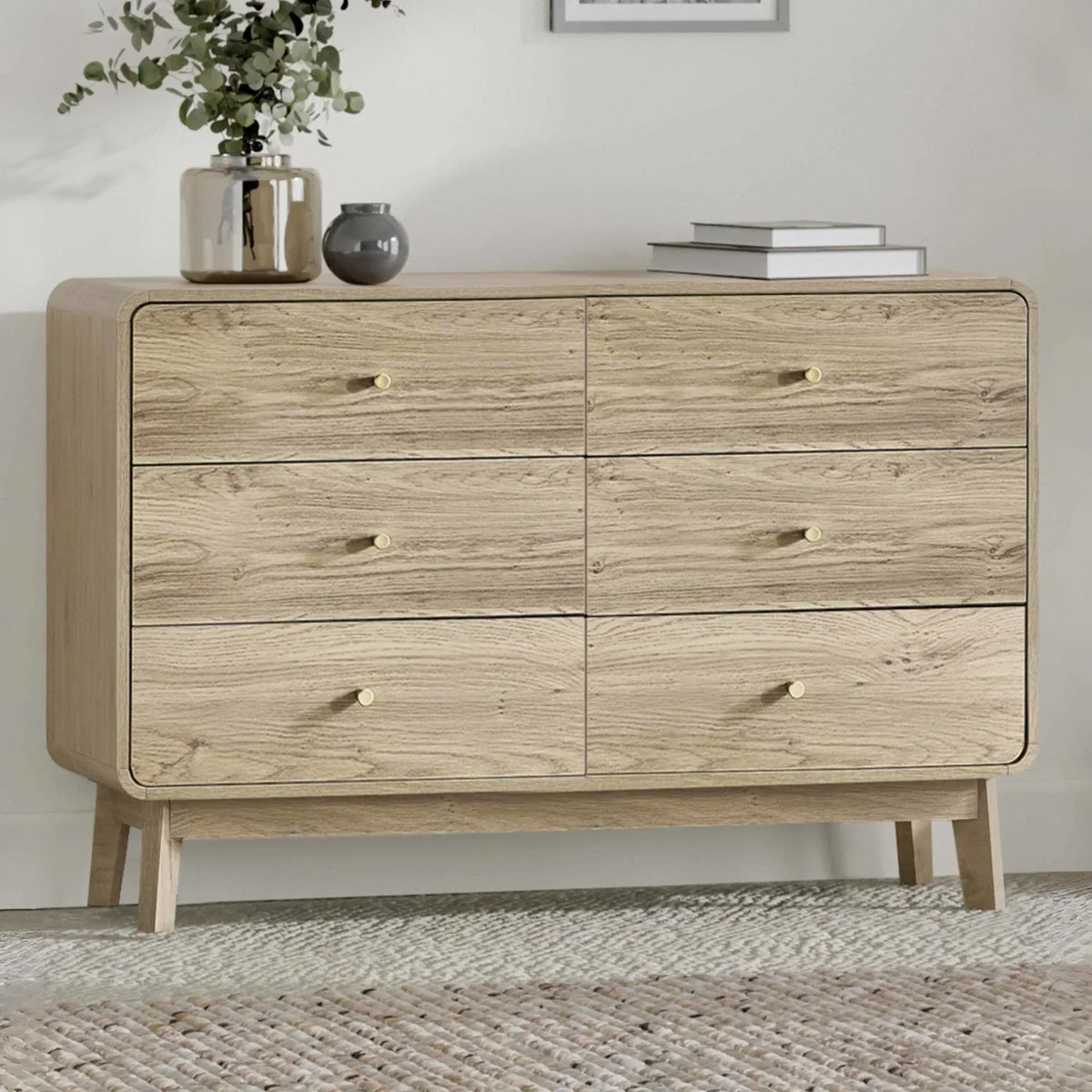 Light oak wood chest of drawers with six drawers and gold knobs, styled with vases on top