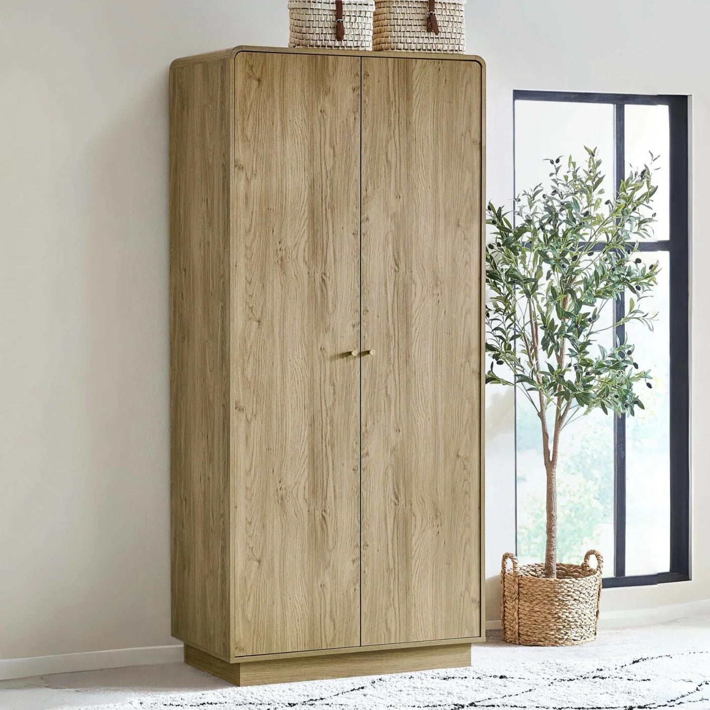 Oak effect wardrobe with gold handle beside window and indoor plant on light rug