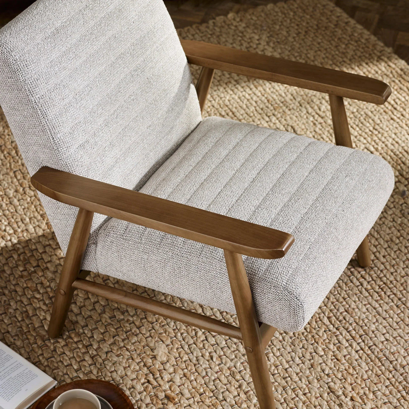 Light beige fabric armchair with wooden arms and legs on woven rug