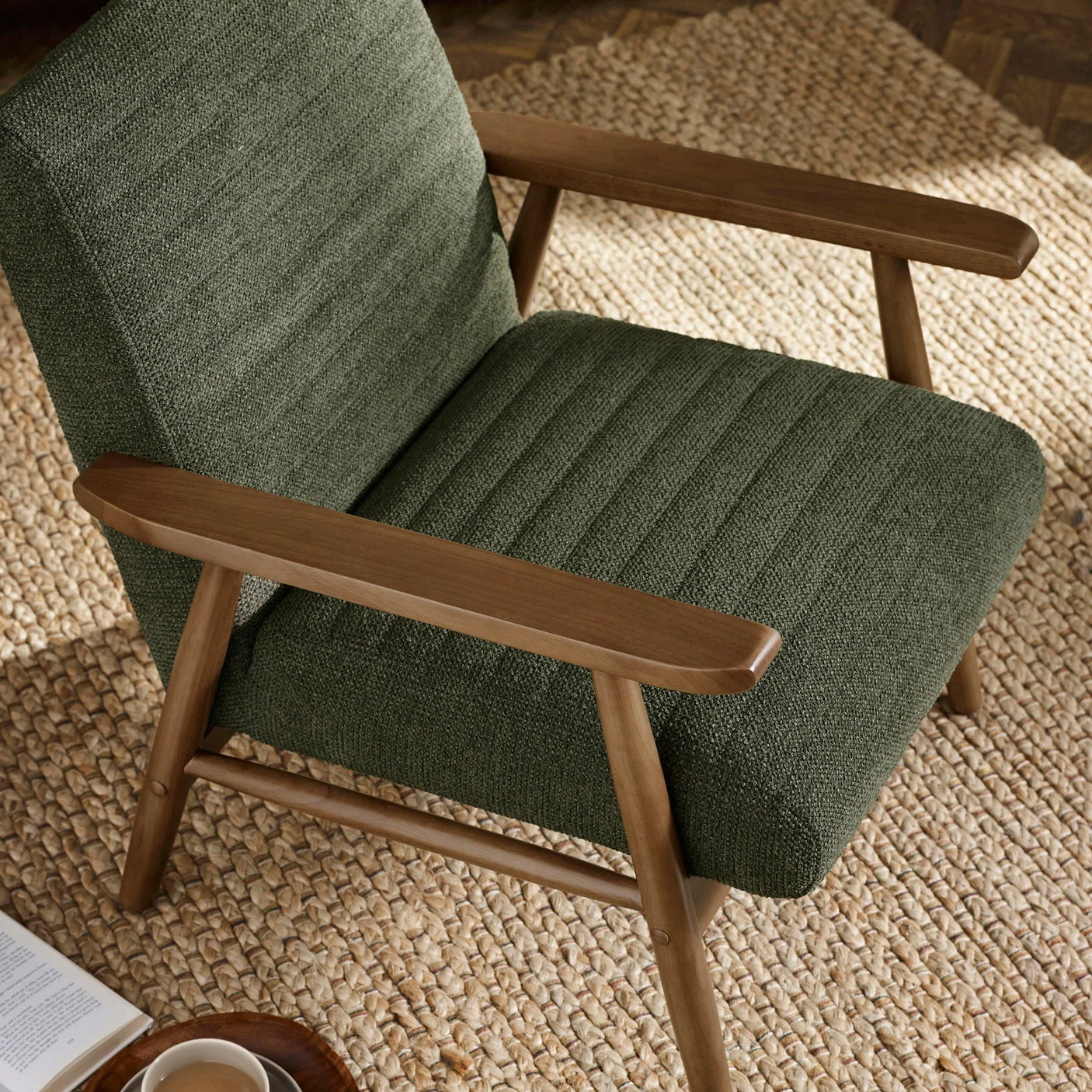 Green fabric armchair with wooden frame on woven rug, close-up of seat and arms