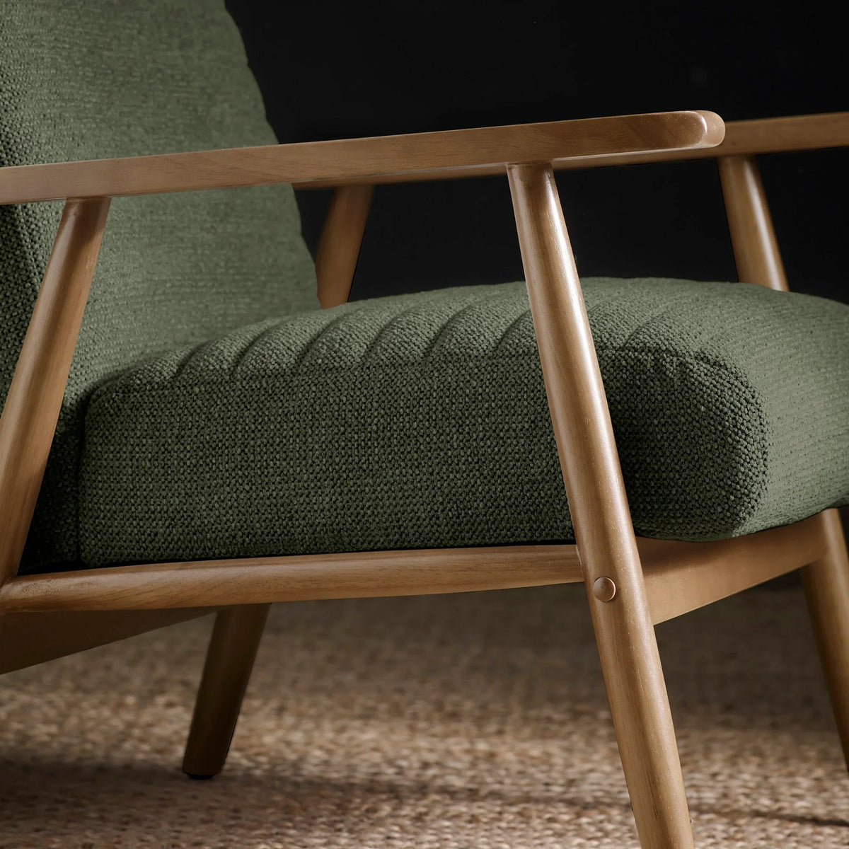 Green fabric accent chair with wooden frame on woven rug, side close-up view