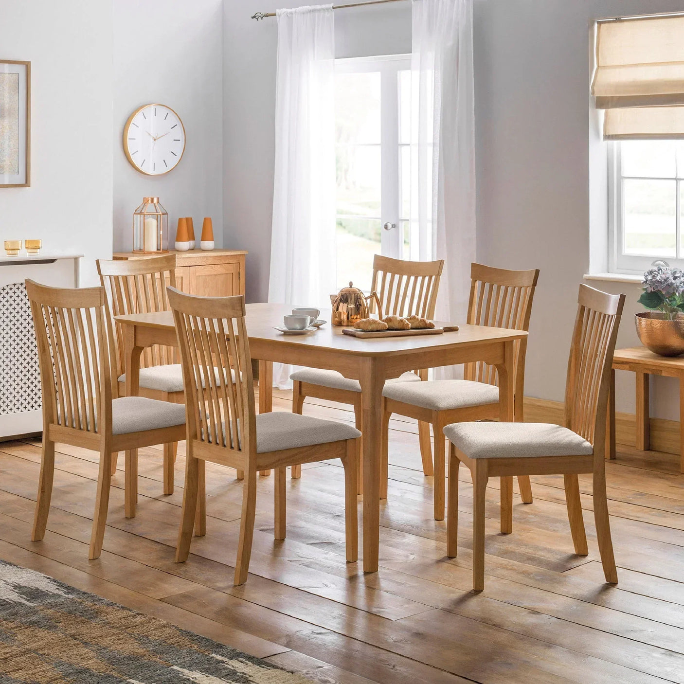 Oak dining table and six slatted back chairs with cream cushions in bright dining room