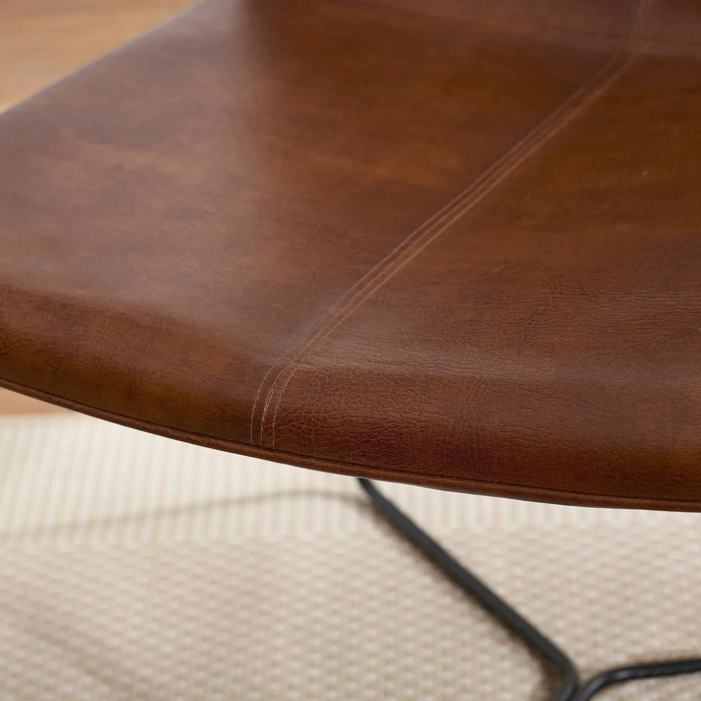 Closeup of brown leather dining chair seat with visible stitching and black metal legs