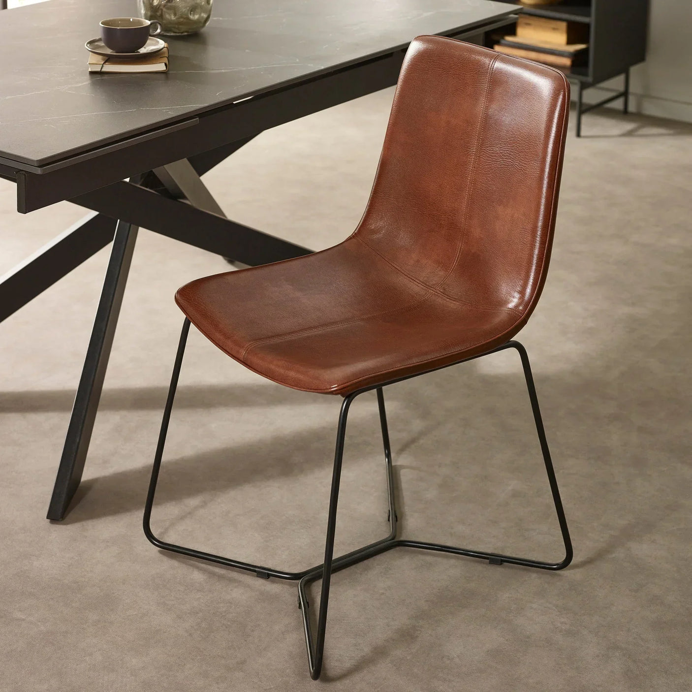 Brown leather dining chair with black metal legs beside modern dining table