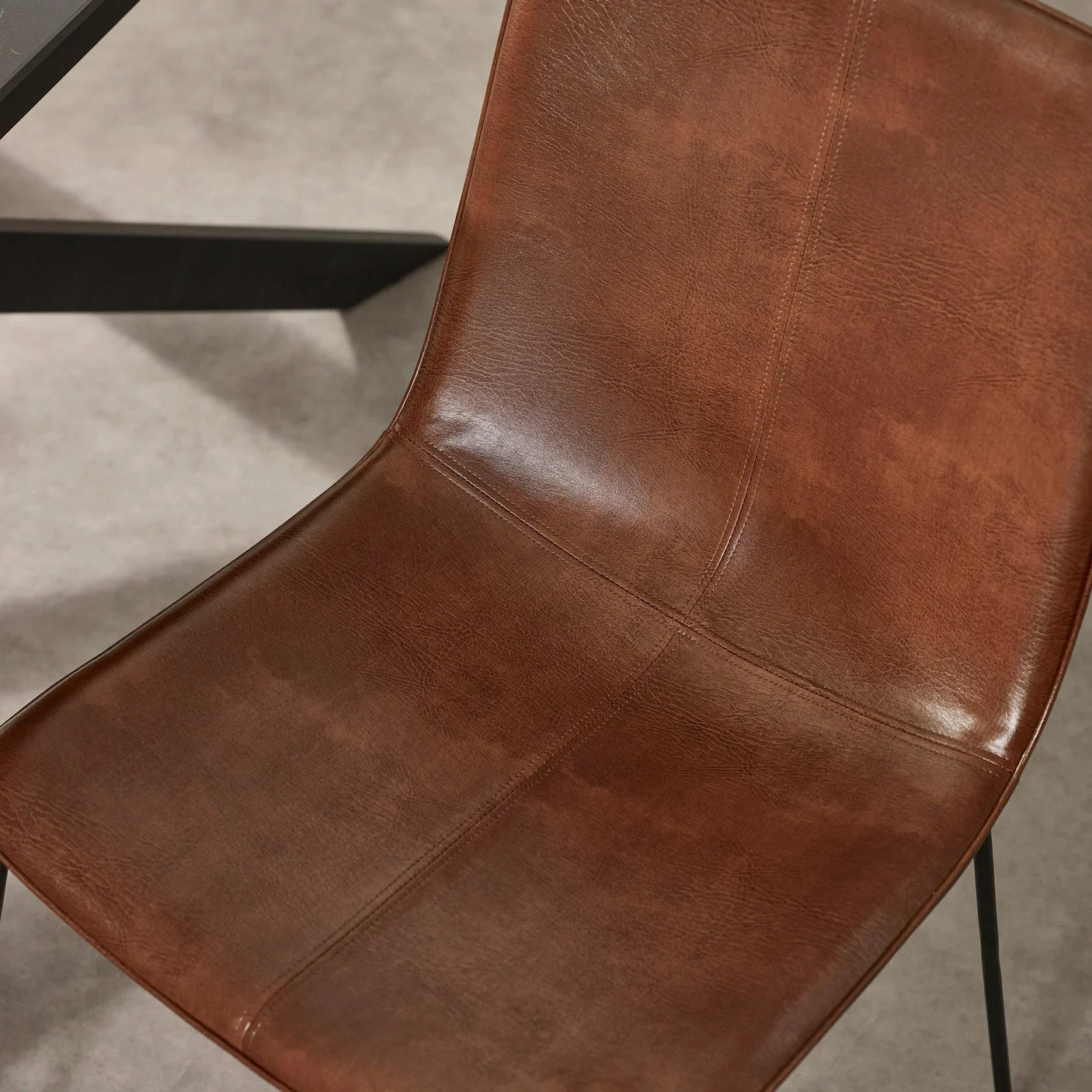 Brown faux leather dining chair with visible stitching and black metal legs