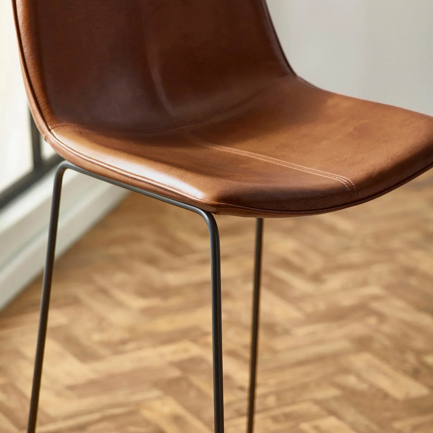 Brown leather dining chair with slim black metal legs on wood parquet floor