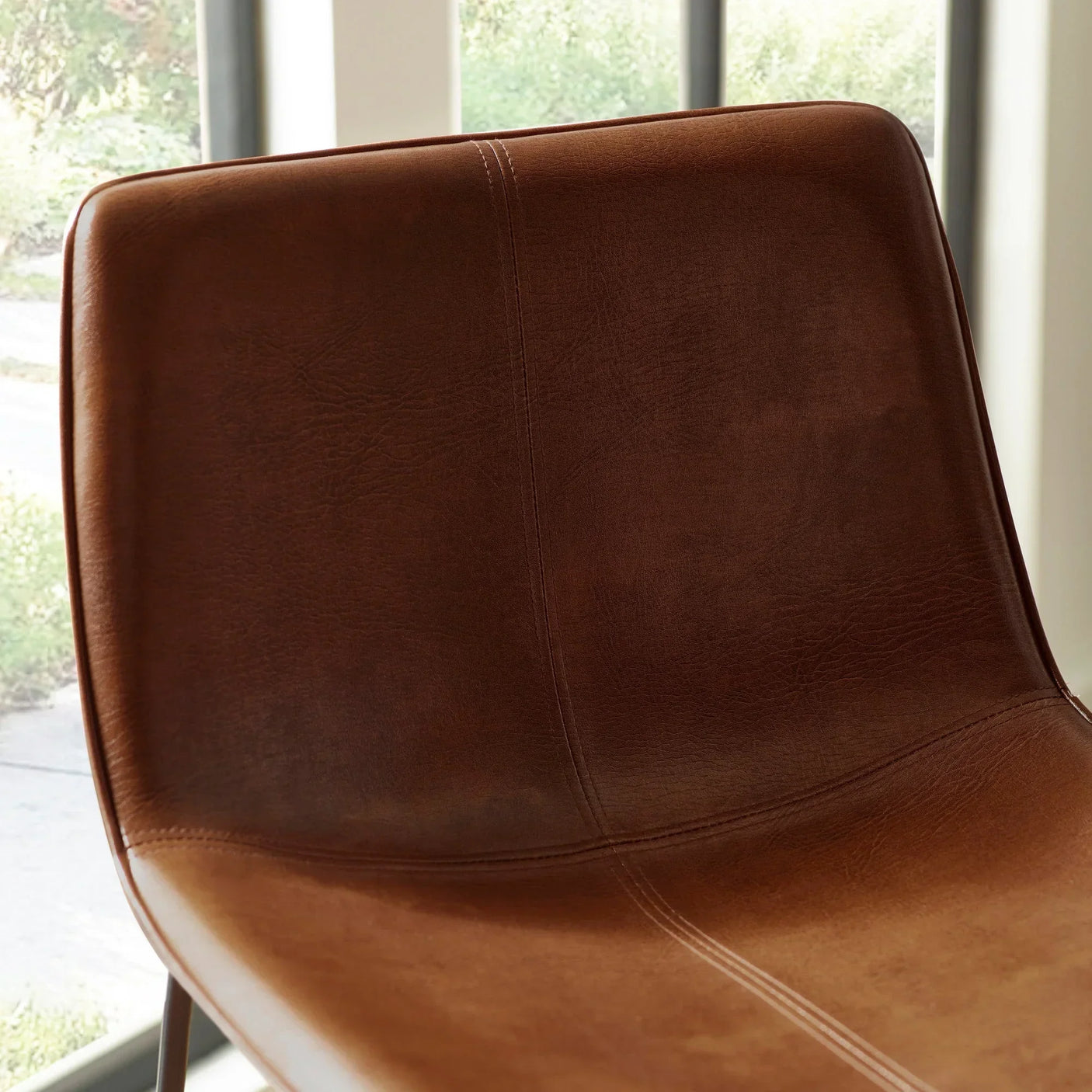 Brown leather dining chair with stitched detail shown in close-up indoor setting