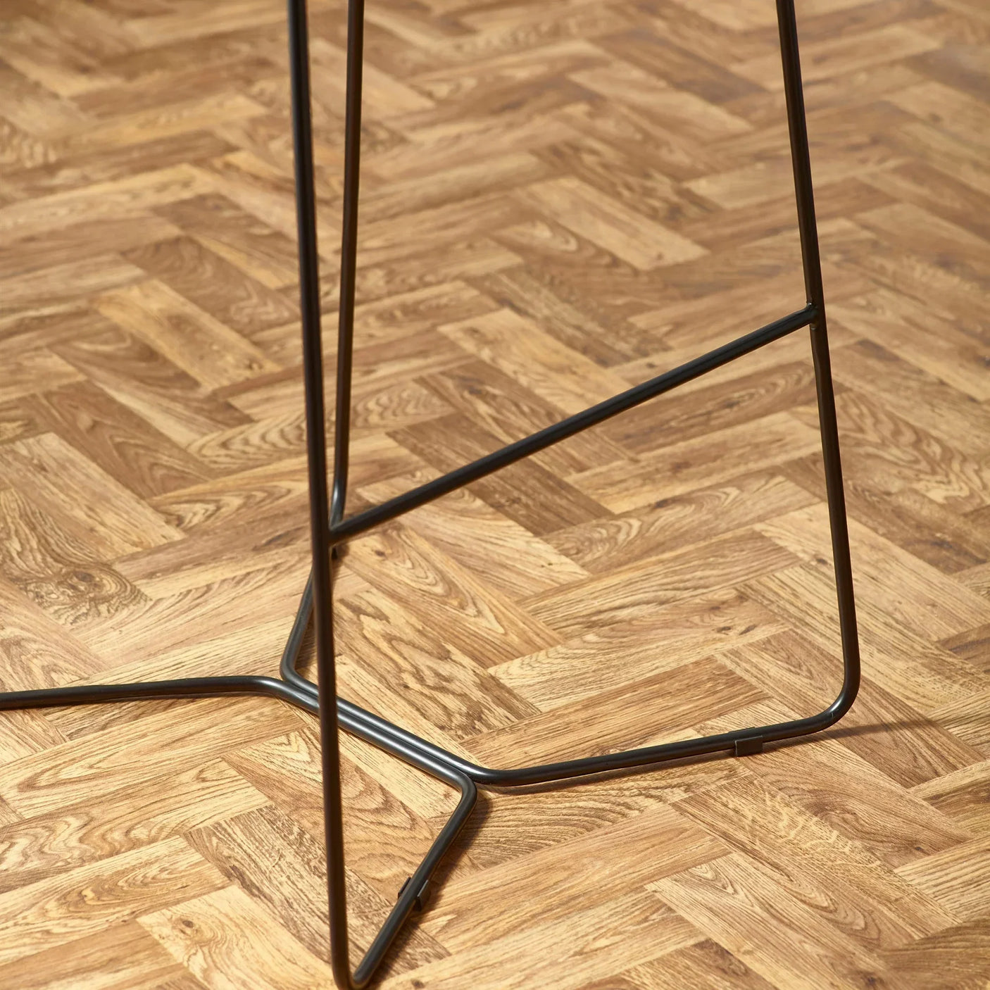 Black metal bar stool frame on herringbone wood floor, close-up of the base and legs