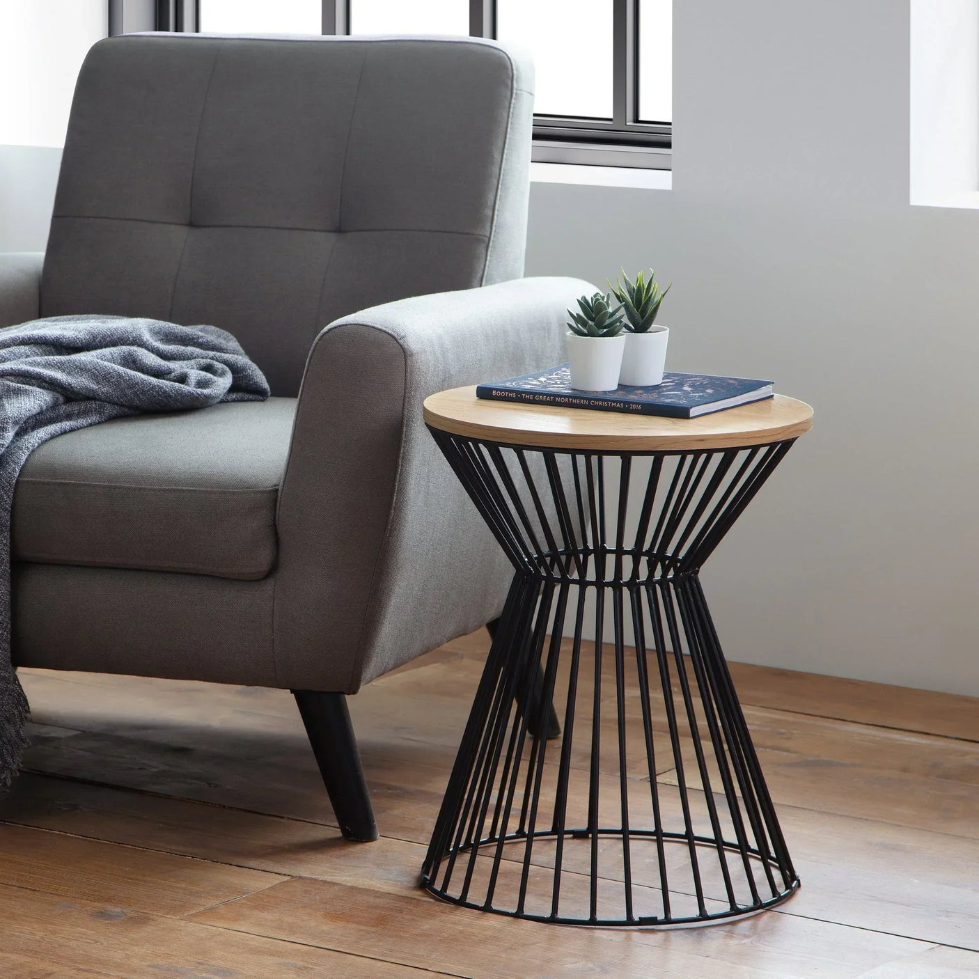 Light oak lamp table with wire base beside grey armchair in living room setting