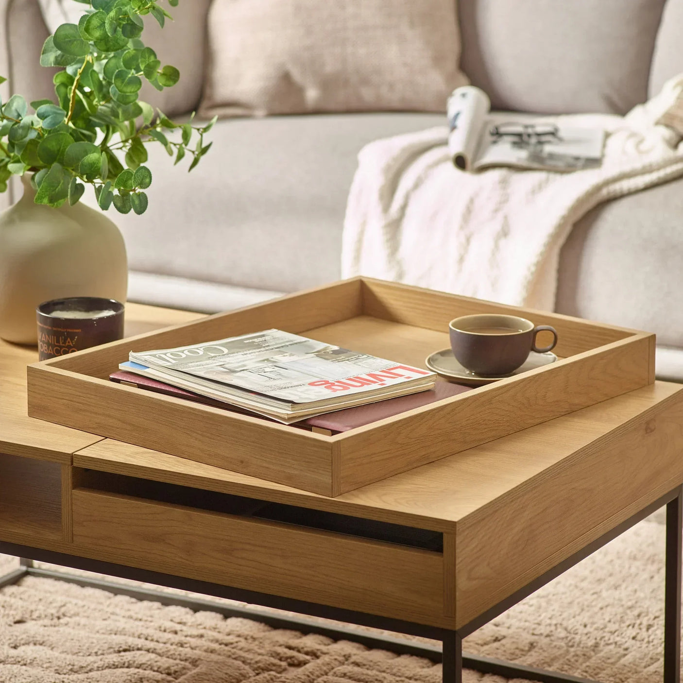 Oak coffee table with magazines, coffee cup and decorative vase in a living room setting