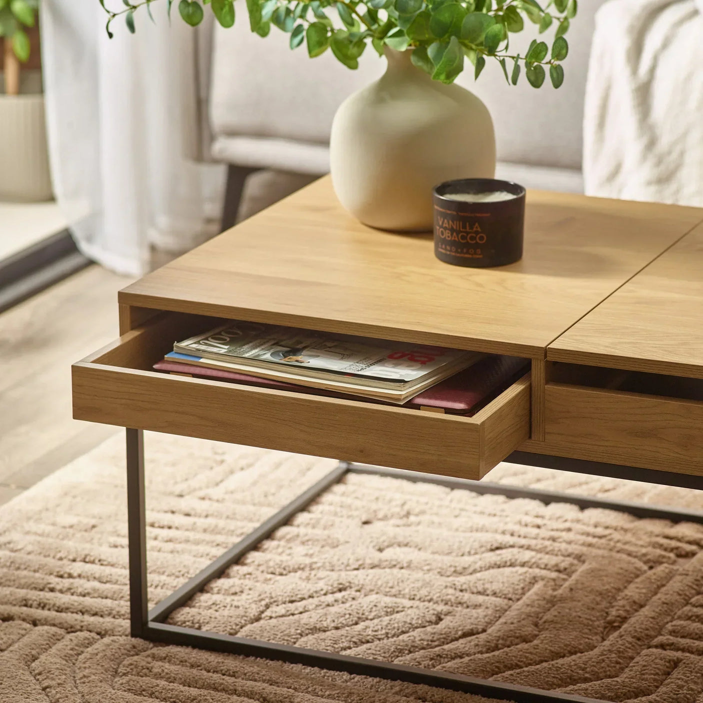 Oak coffee table with open drawer, metal legs, vase and candle on textured rug