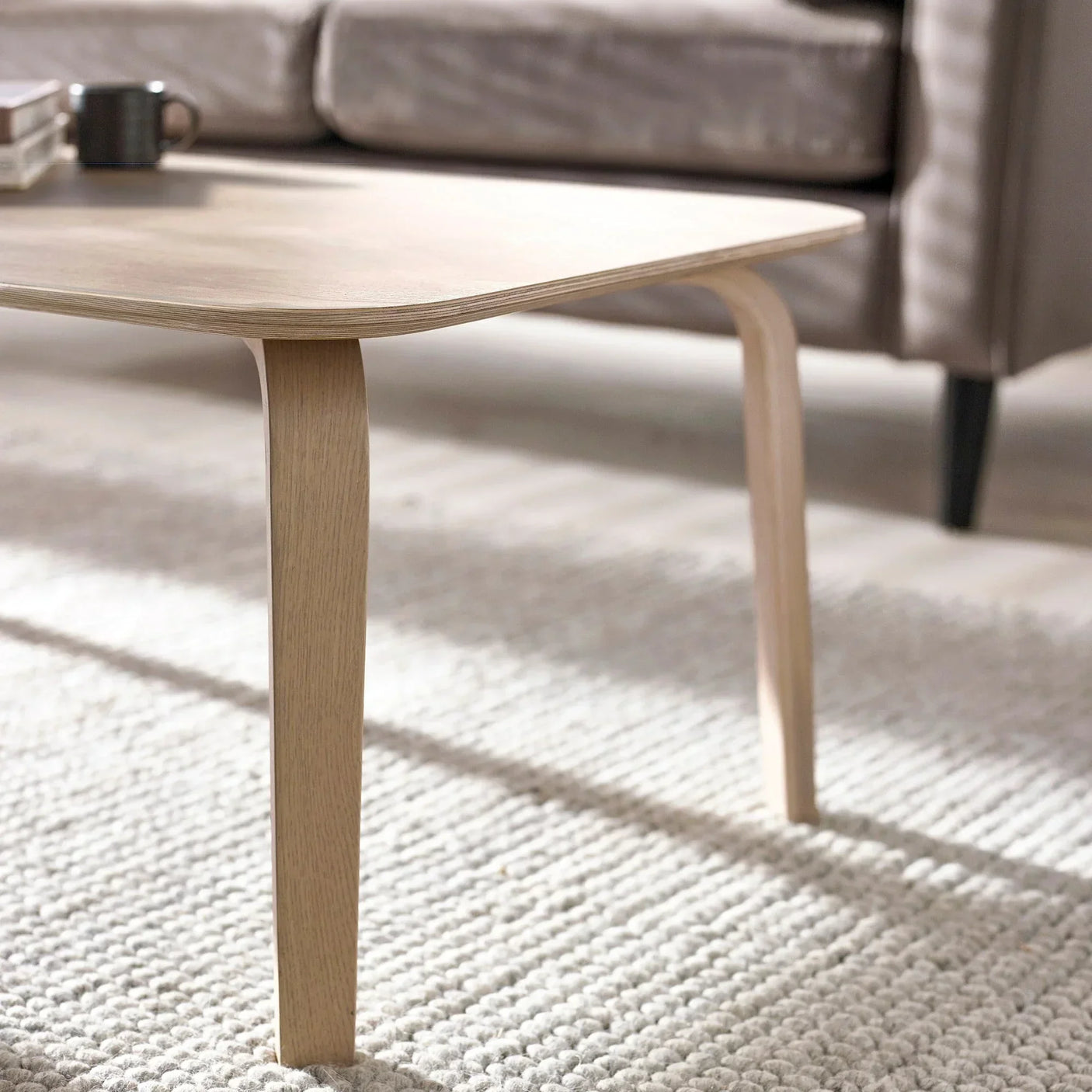 Light wood coffee table with curved legs on textured rug in modern living room setting