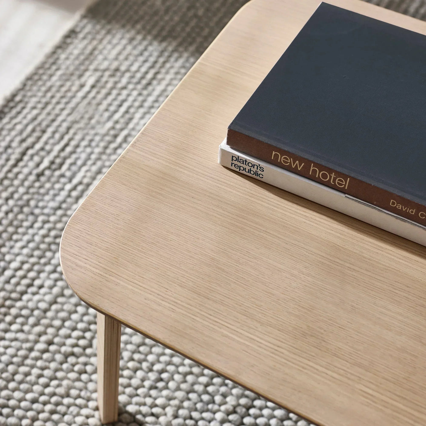 Light wood coffee table with rounded corner, two books on surface, textured rug below