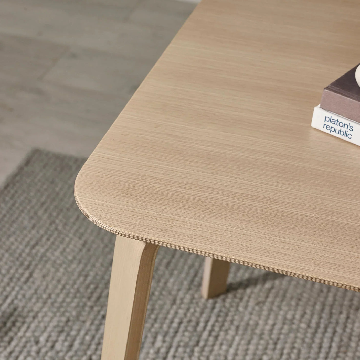Close-up of light wood coffee table corner with book and textured rug underneath