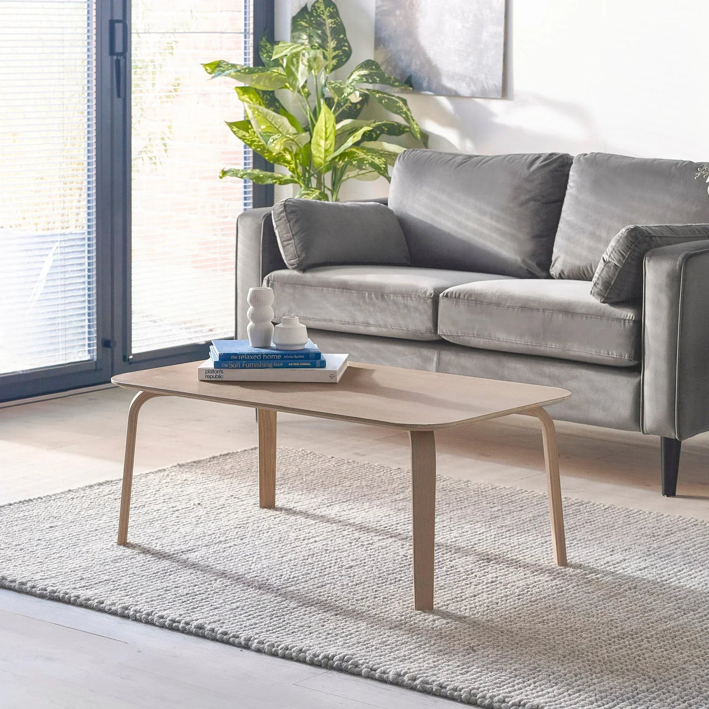 Light wood coffee table with curved legs on grey rug in modern living room