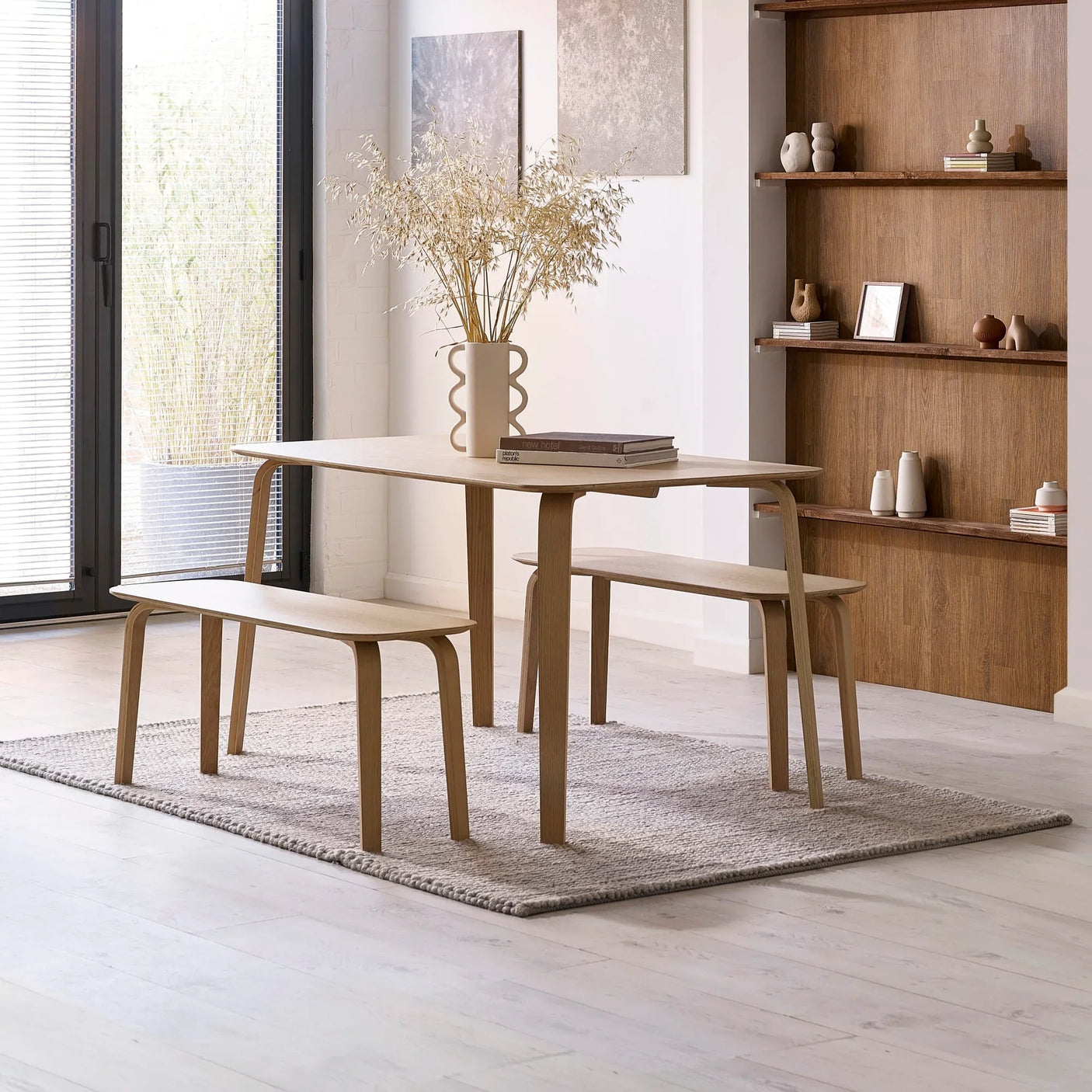 Oak dining table with matching benches on grey rug in modern living space with natural light