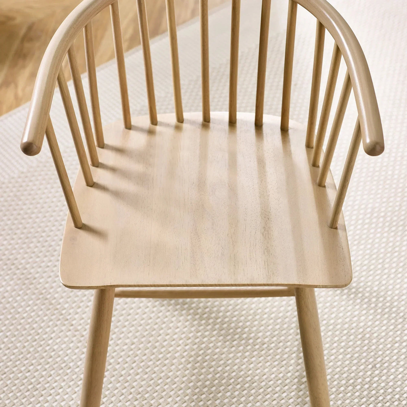 Natural wood dining chair with spindle backrest on textured rug