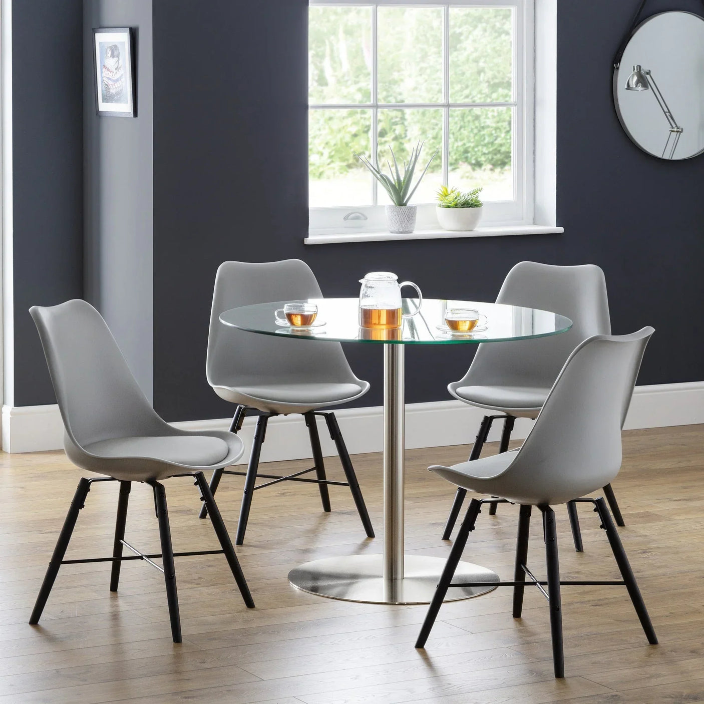 Grey dining chairs with black legs around a glass table in a modern dining room setting