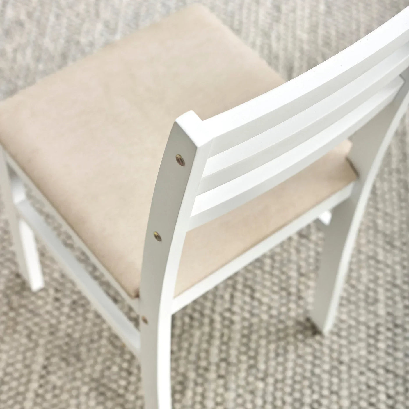 White wooden dining chair with beige upholstered seat on textured rug