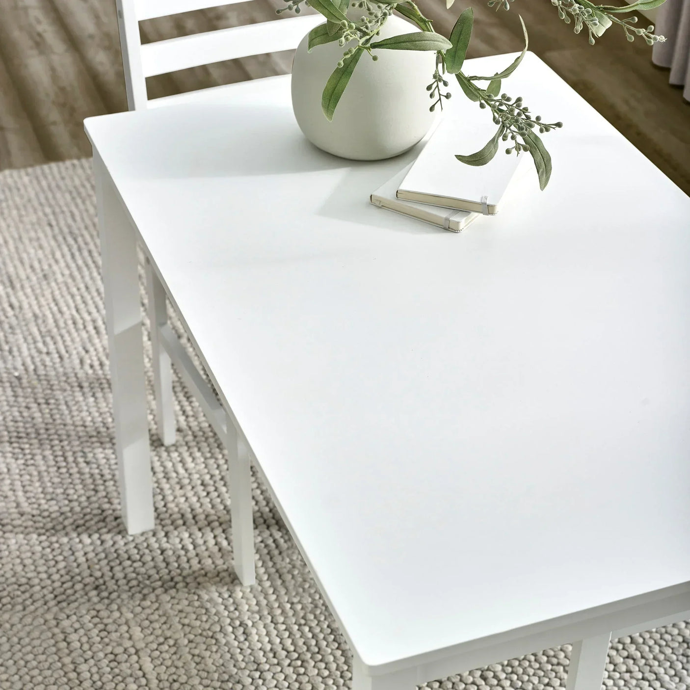 White dining table with matching chair, potted plant, and notebooks on textured rug