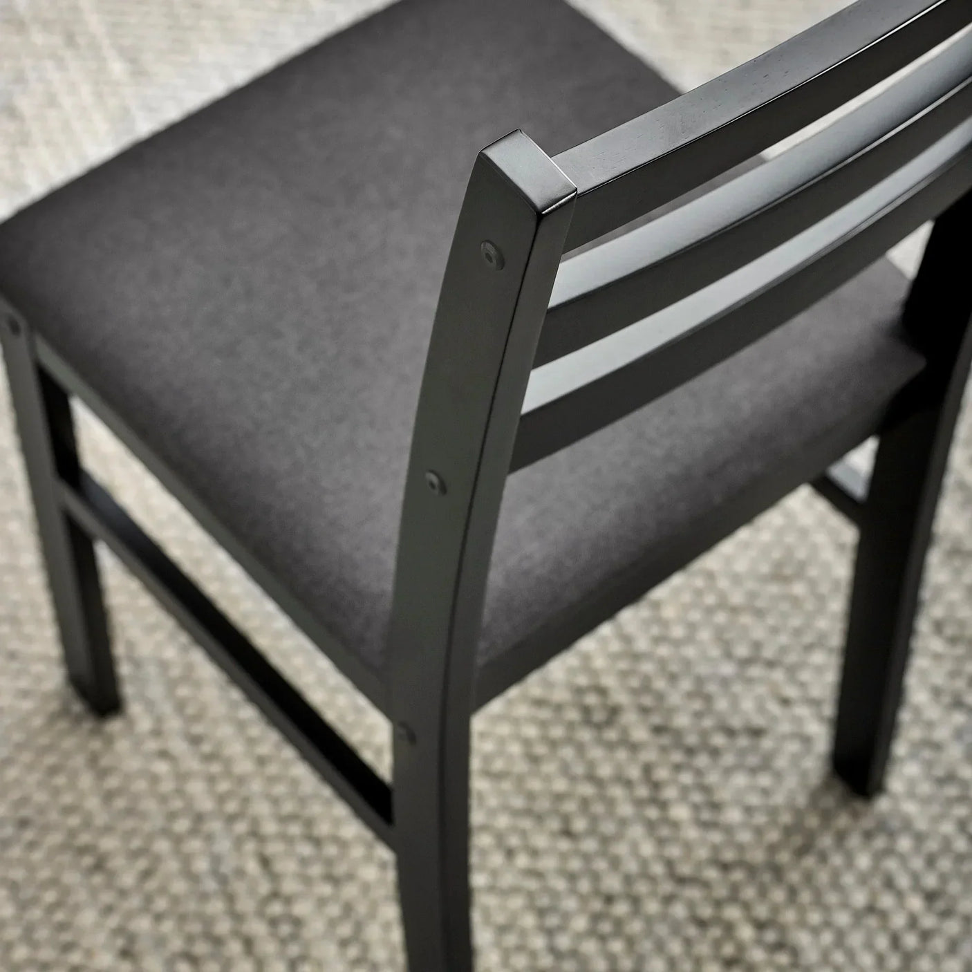 Black dining chair with cushioned grey seat and slatted backrest on textured carpet