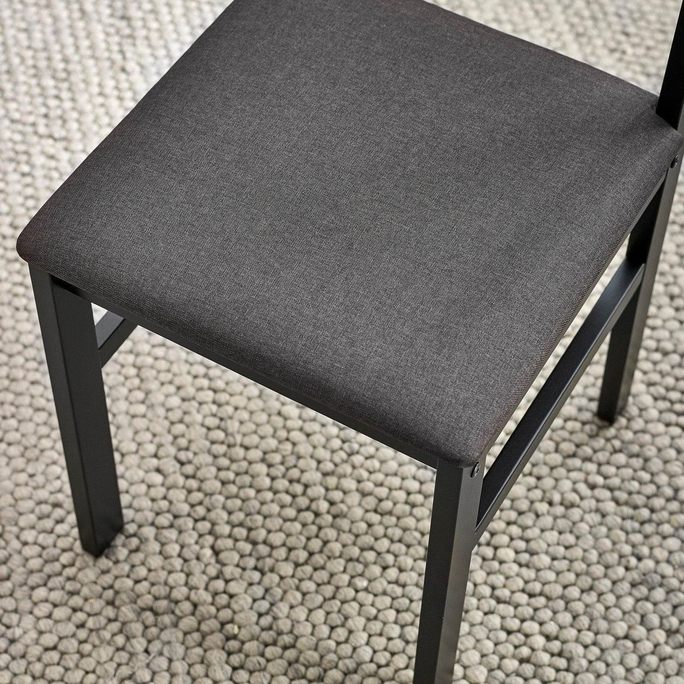 Grey fabric dining chair with black metal legs on textured rug