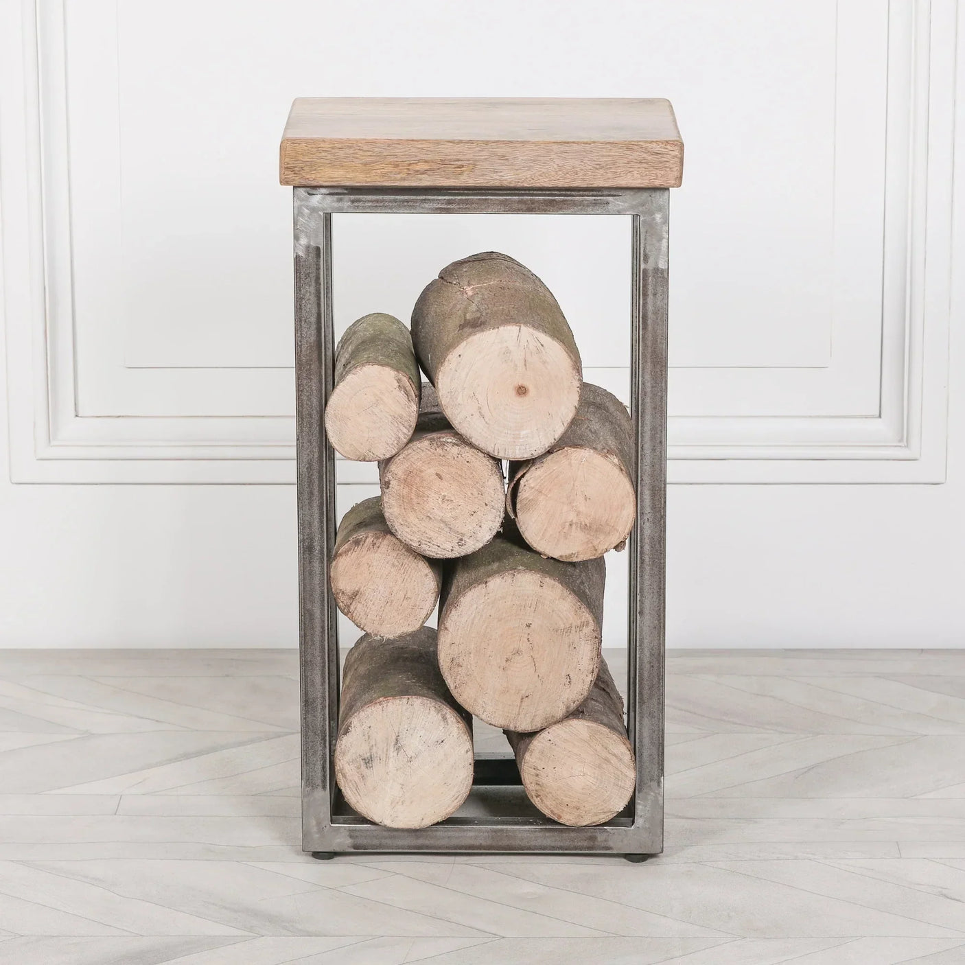 Metal log holder with wood top, filled with firewood, against white wall and light floor