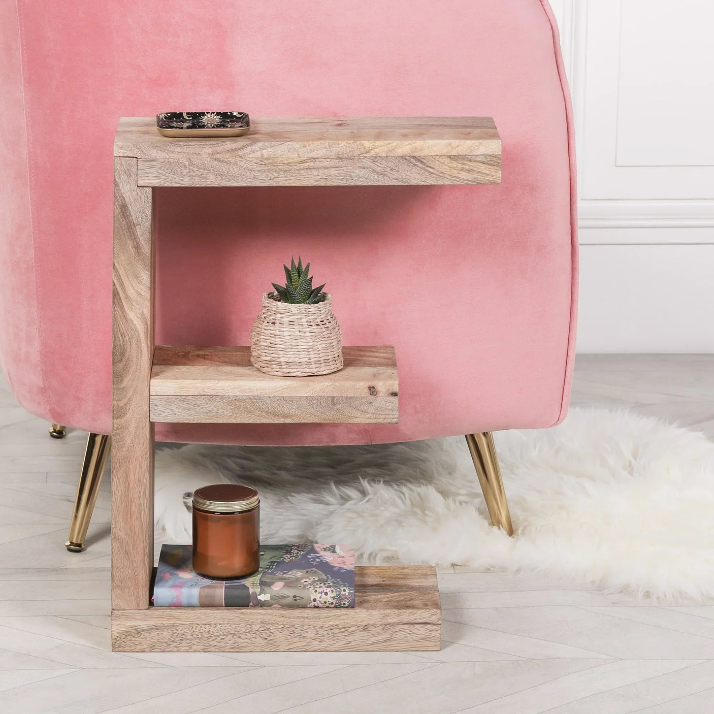 Mango wood side table with three shelves beside pink velvet chair and white rug